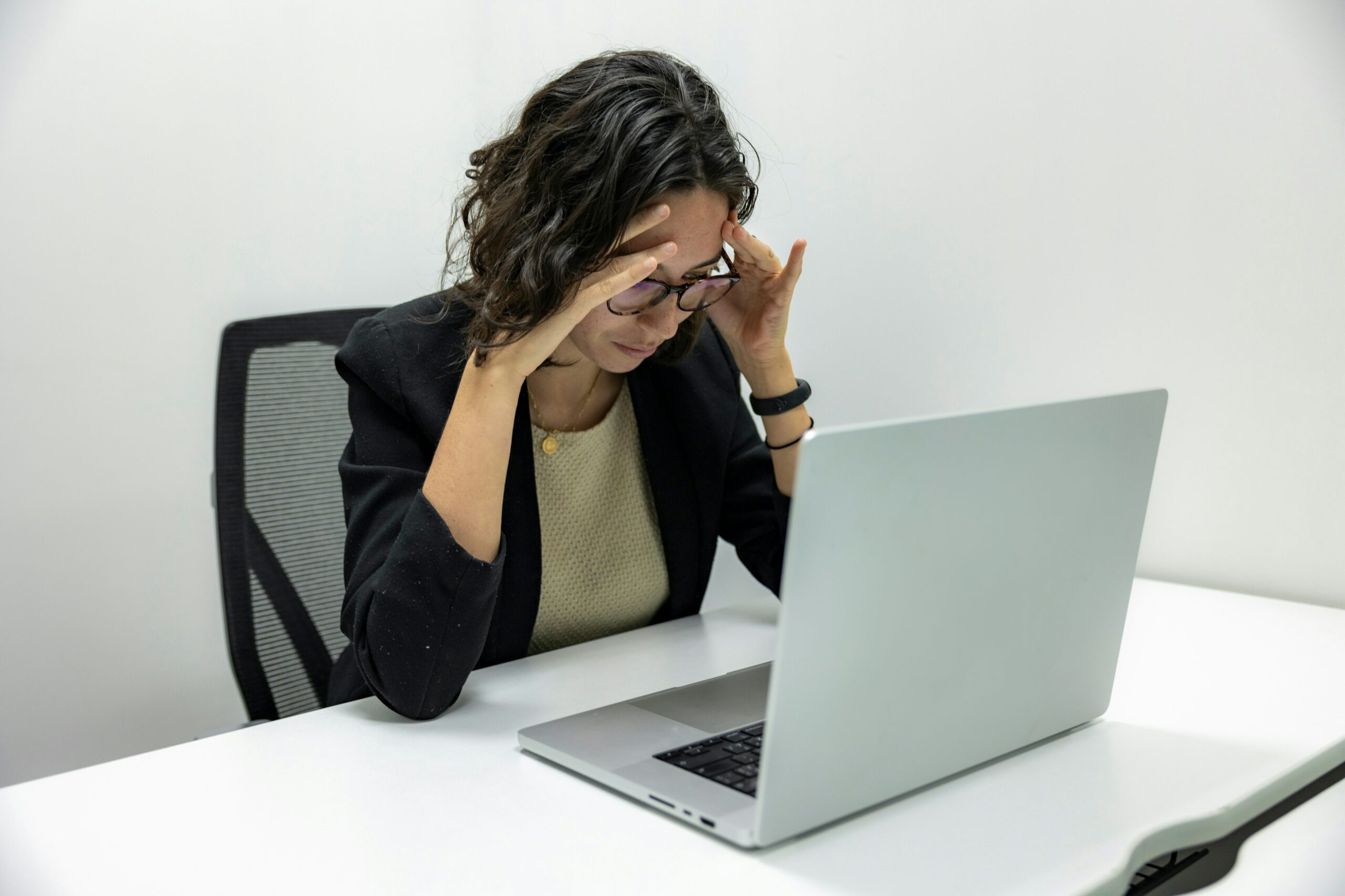 Woman places her head in her hands in front of her computer and appears stressed at work.